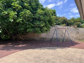 A playground with a swing set and a paved area. - Gîte Le Clocher du Layon (Nueil Sur Layon)