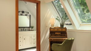 Una habitación con tragaluz, un escritorio de madera, una silla verde, un espejo y un armario blanco.