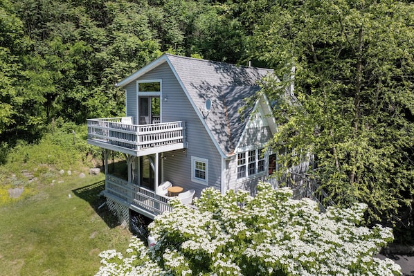 A two-story house with a balcony, surrounded by lush greenery.