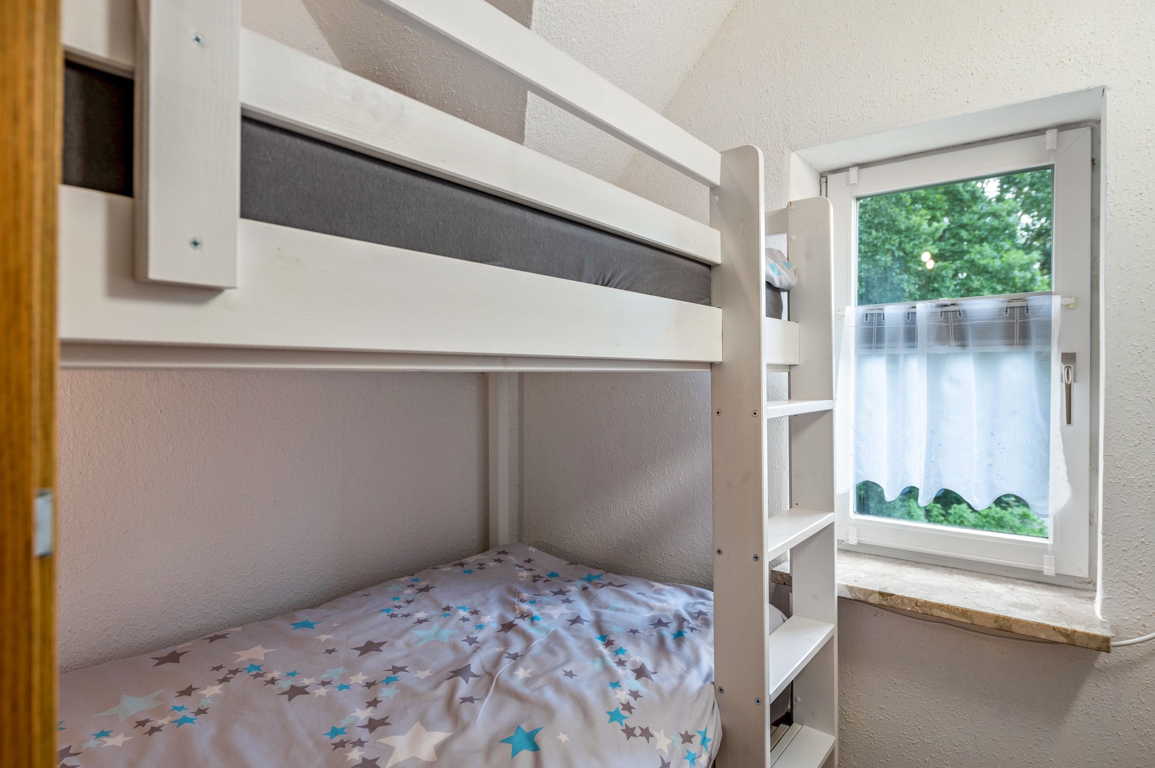 Ein Etagenbett mit Fenster darüber, ein Nachttisch und ein Bett mit Sternenmuster.
