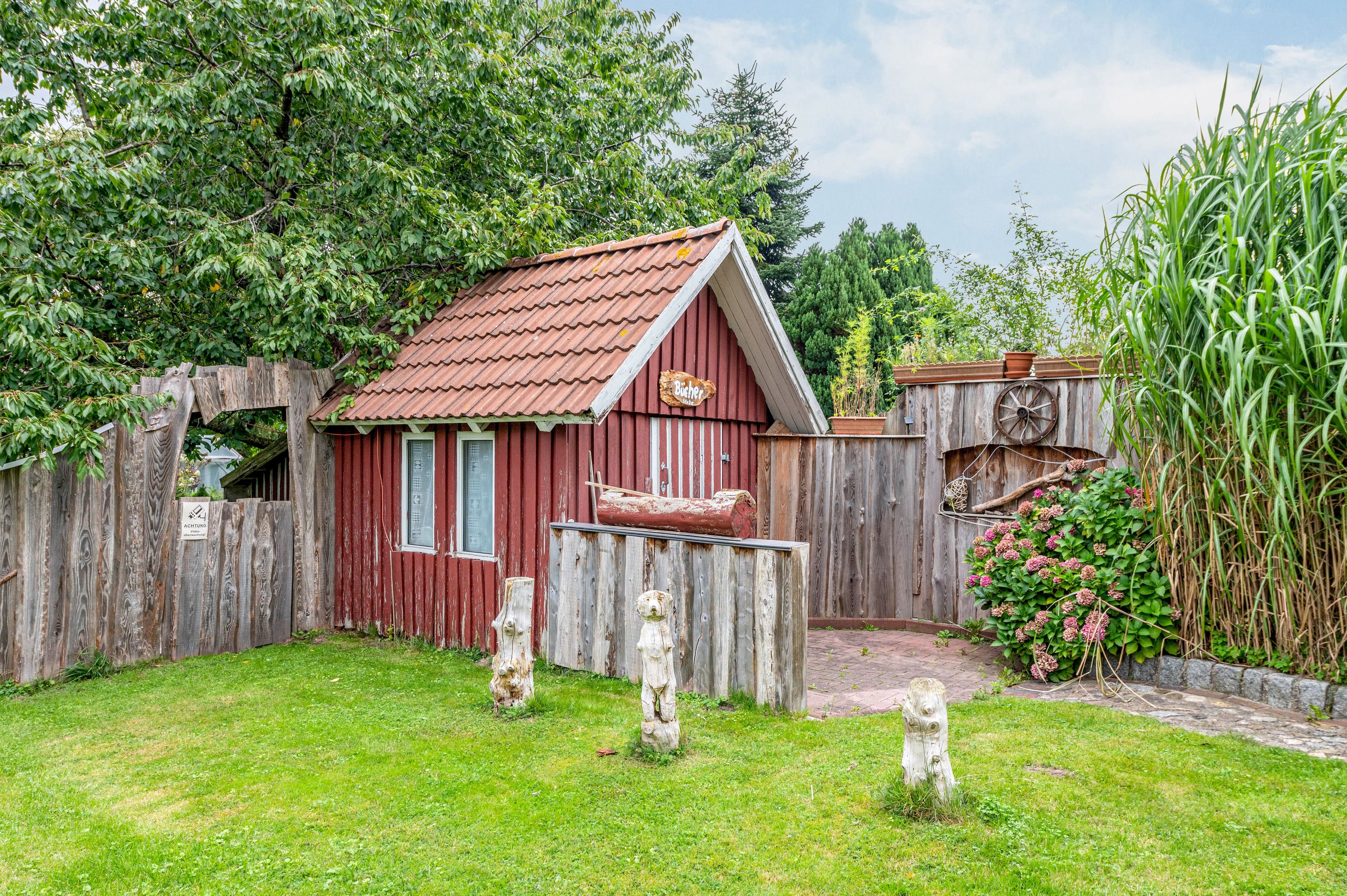Ein rotes Holzgebäude mit geneigtem Dach, umgeben von einem Holzzaun und einem Rasen.