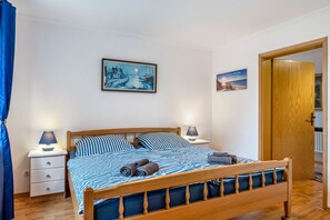 Ein Schlafzimmer mit einem hölzernen Bett, zwei Nachttischen mit Lampen, einer blau-weißen Bettdecke und zwei gerahmten Bildern an der Wand.