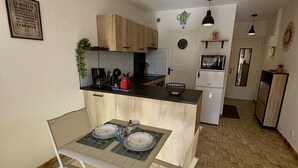 A compact kitchen with a dining area, a microwave, a refrigerator, and a clock on the wall. - Well-located, quiet studio with a pool (Gruissan)