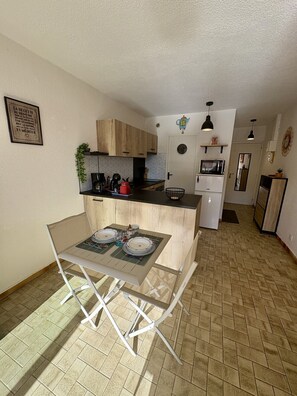 A compact kitchen with a dining area, a microwave, a refrigerator, and a clock on the wall. - Well-located, quiet studio with a pool (Gruissan)