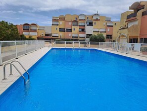A swimming pool with a white fence, surrounded by multi-story buildings. - Well-located, quiet studio with a pool (Gruissan)