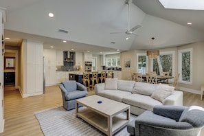 A spacious living area with a sofa, armchairs, and a coffee table. A kitchen with white cabinets and a dining area with a table and chairs are visible. - 3 Jessamine - A Coastal Comfort Escape Available Starting August 2026! (Hilton Head Island)