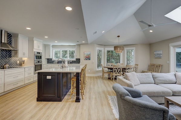 A spacious kitchen with modern appliances, a dining area with wooden chairs, and a large window providing natural light. - 3 Jessamine - A Coastal Comfort Escape Available Starting August 2026! (Hilton Head Island)