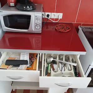 A kitchen with a microwave, a red countertop, and a drawer with utensils. - Charming little one-bedroom-plus apartment in Verdon-sur-Mer, right near the beaches (Le Verdon-sur-Mer)