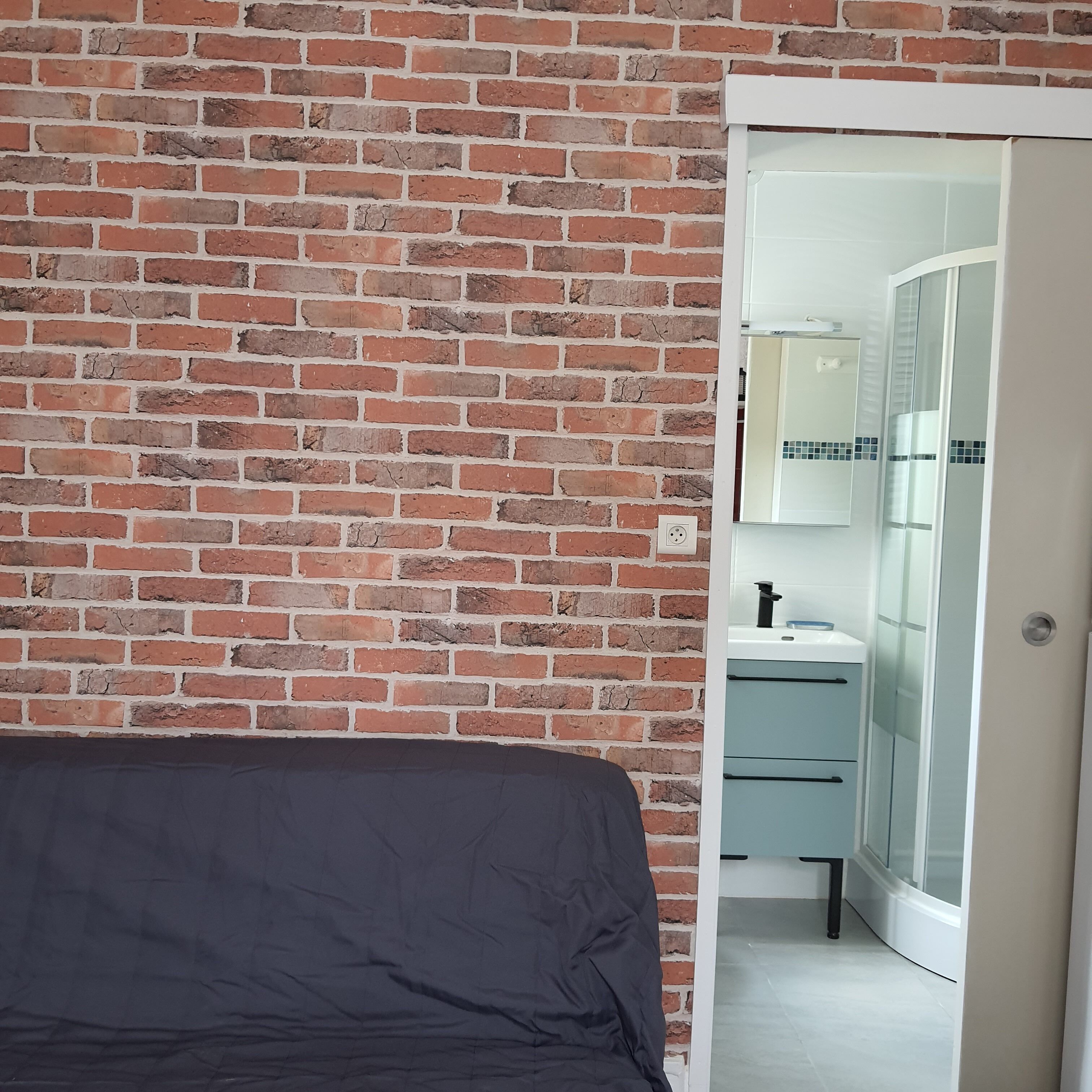 A room with a brick wall, a bed, and a bathroom with a mirror and sink.