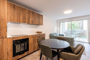 A modern kitchen with wooden cabinets, a built-in oven, and a dining area with a round table and chairs. - CIMES B105C  By Avecoeur (Briançon)