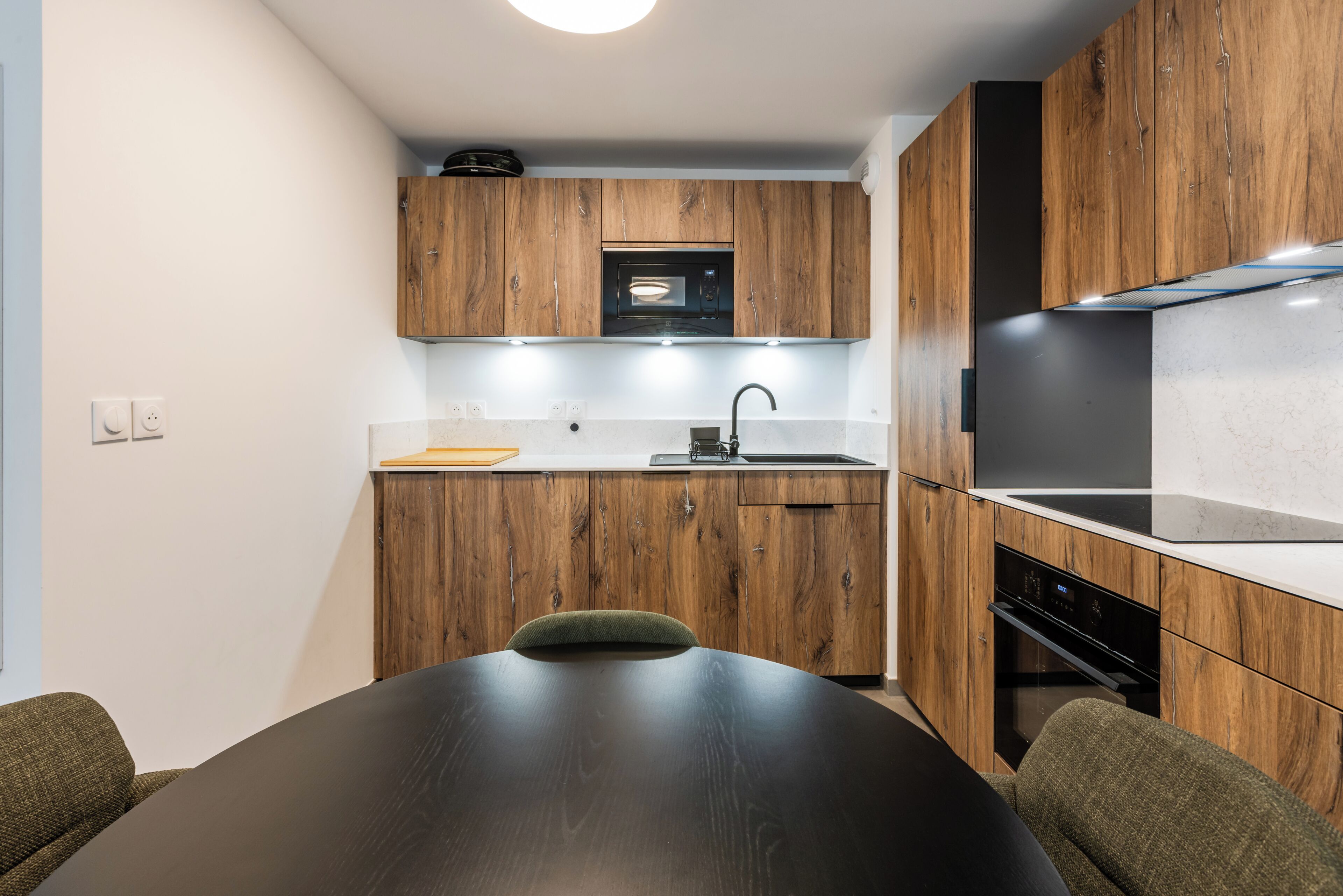 A modern kitchen with wooden cabinets, a built-in oven, and a dining area with a table and chairs.