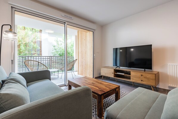 A modern living room with a sofa, a coffee table, a TV on a wooden cabinet, and a sliding glass door leading to an outdoor area. - CIMES B105C  By Avecoeur (Briançon)