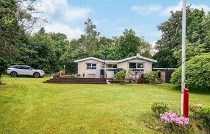 A two-story house with a front deck, a barbecue area, and a car parked in the driveway. - 4 bedroom gorgeous home in Højslev (Højslev)