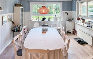 A dining area with a long table, white chairs, a hanging light fixture, and a window with a view of greenery. - 4 bedroom gorgeous home in Højslev (Højslev)