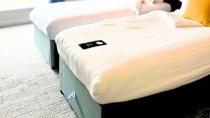 Habitación de hotel con dos camas, un ventanal con cortinas, un ventilador de techo y un cuadro en la pared.