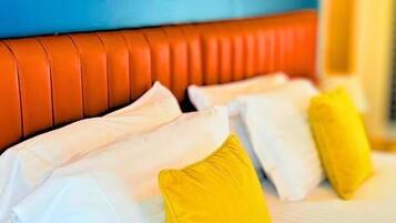 A bed with white linens and yellow pillows, a blue wall, and a framed picture above the bed.