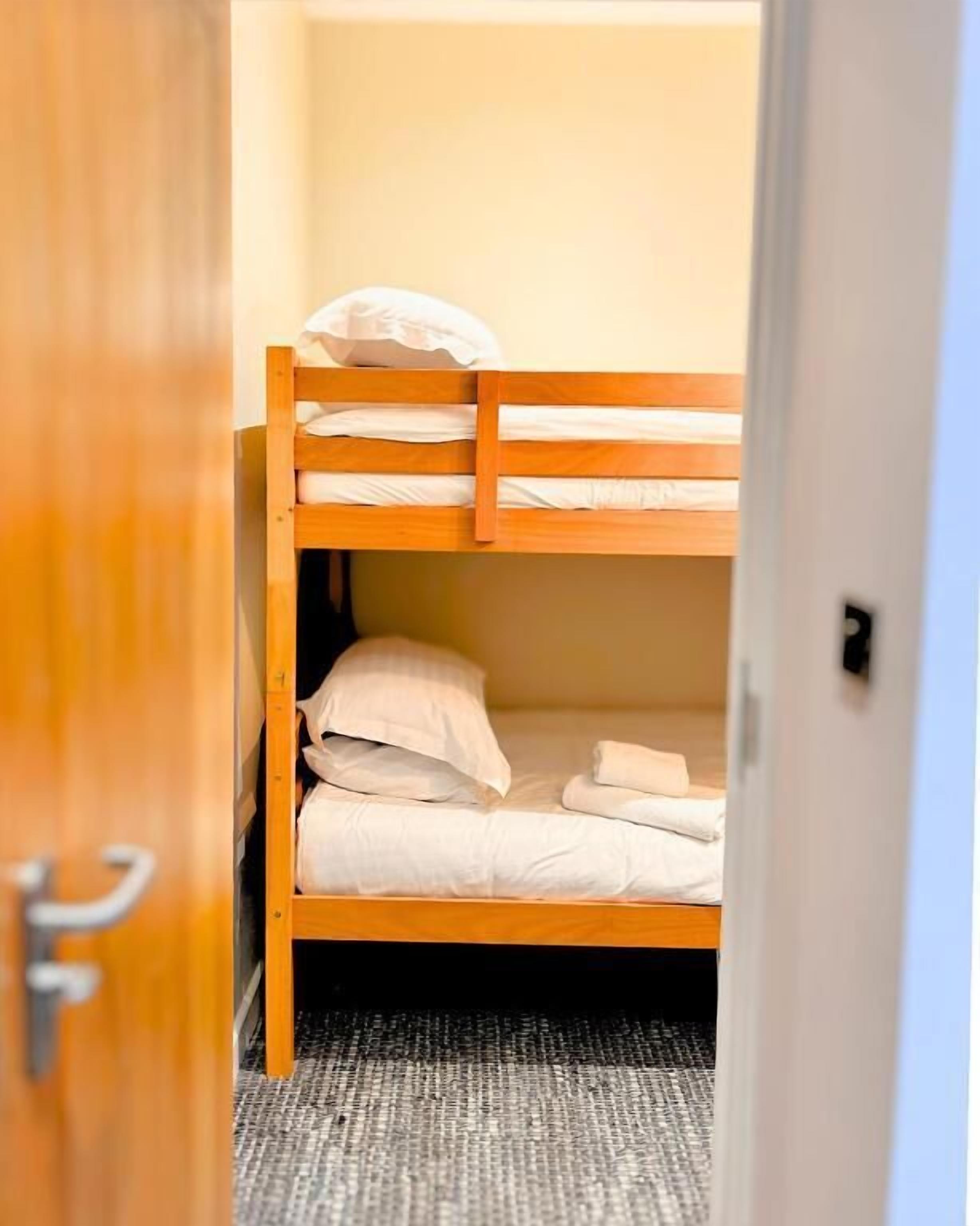 Une chambre avec un lit superposé, une structure en bois, une porte et un sol recouvert de moquette.