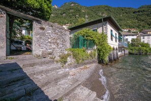 Ein Steinhaus mit Balkon, einem Fluss und einem Berg im Hintergrund.