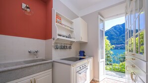 Eine Küche mit weißen Schränken, einer Arbeitsplatte aus Granit, einem eingebauten Ofen und Blick auf eine gebirgige Landschaft durch eine offene Tür.