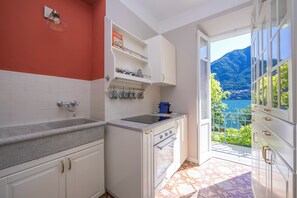 Eine Küche mit weißen Schränken, einer Arbeitsplatte aus Granit, einem eingebauten Ofen und Blick auf eine gebirgige Landschaft durch eine offene Tür.