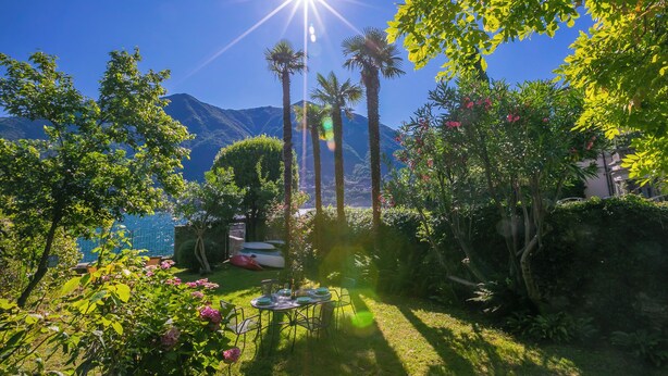 Ein Garten mit Tisch und Stühlen, Palmen und einem Berg im Hintergrund.