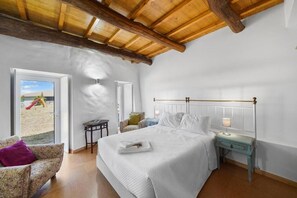 Ein Schlafzimmer mit Bett, Nachttisch, Lampe, Stuhl und Blick ins Freie.