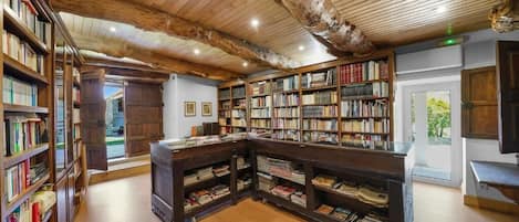 A library with wooden bookshelves, a central table, and a rustic ceiling.