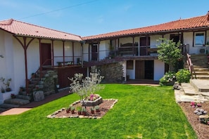 A two-story building with a red-tiled roof, a stone staircase, and a small garden area with potted plants.