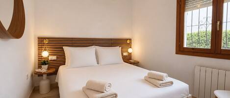 Une chambre à coucher comprenant un lit, des lampes de chevet, une fenêtre, un radiateur et un climatiseur fixé au mur.