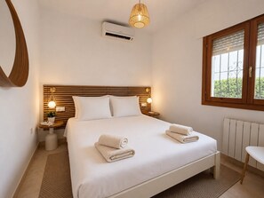 Ein Schlafzimmer mit einem Bett, Nachttischlampen, einem Fenster, einer Heizung und einer Wand-Klimaanlage.