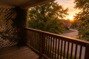 Une terrasse en bois avec une clôture en treillis, donnant sur une rue résidentielle au coucher du soleil.