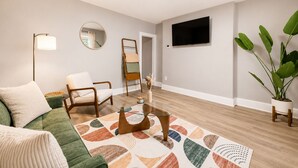 A living room with a sofa, armchair, coffee table, floor lamp, mirror, TV, and a potted plant. - Modern 2BD 1BA Near OSU Fairgrounds FREE Parking (Columbus)