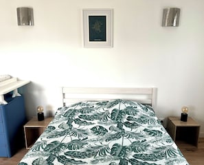 Ein Schlafzimmer mit einem Bett, Nachttischen, einem gerahmten Bild an der Wand und einem blauen Sessel.