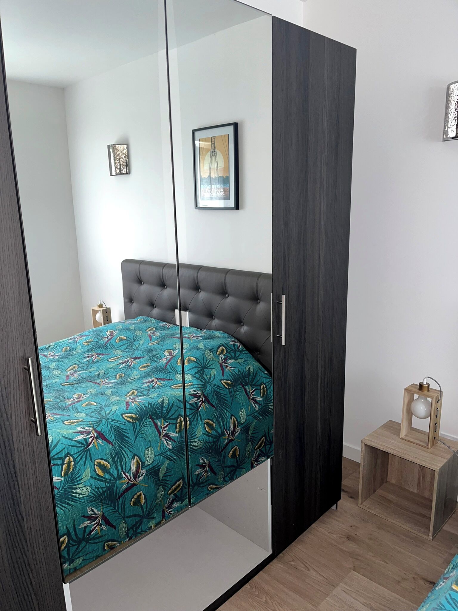 A bedroom with a bed, a wardrobe, a small bedside table, and a framed picture on the wall.