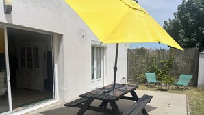 A patio with a wooden table and chairs, a yellow umbrella, and a sliding glass door leading to an interior space.