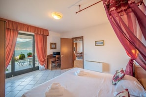 Ein Hotelzimmer mit Bett, Schreibtisch, Stuhl, einem Balkon mit Blick und einer Tür zu einem weiteren Raum.