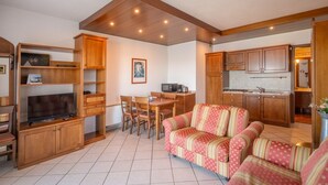 A compact living space with a sofa, TV, wooden cabinets, a dining area, and a kitchenette. - ApartmentsGarda - Villa Giada - RUBINO (TORRI DEL BENACO)