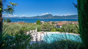 A pool with a view of the sea and mountains, surrounded by greenery and buildings. - ApartmentsGarda - Villa Giada - RUBINO (TORRI DEL BENACO)