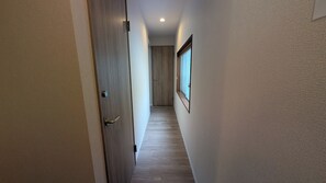 Un pasillo estrecho con una puerta de madera a la izquierda y una ventana a la derecha.