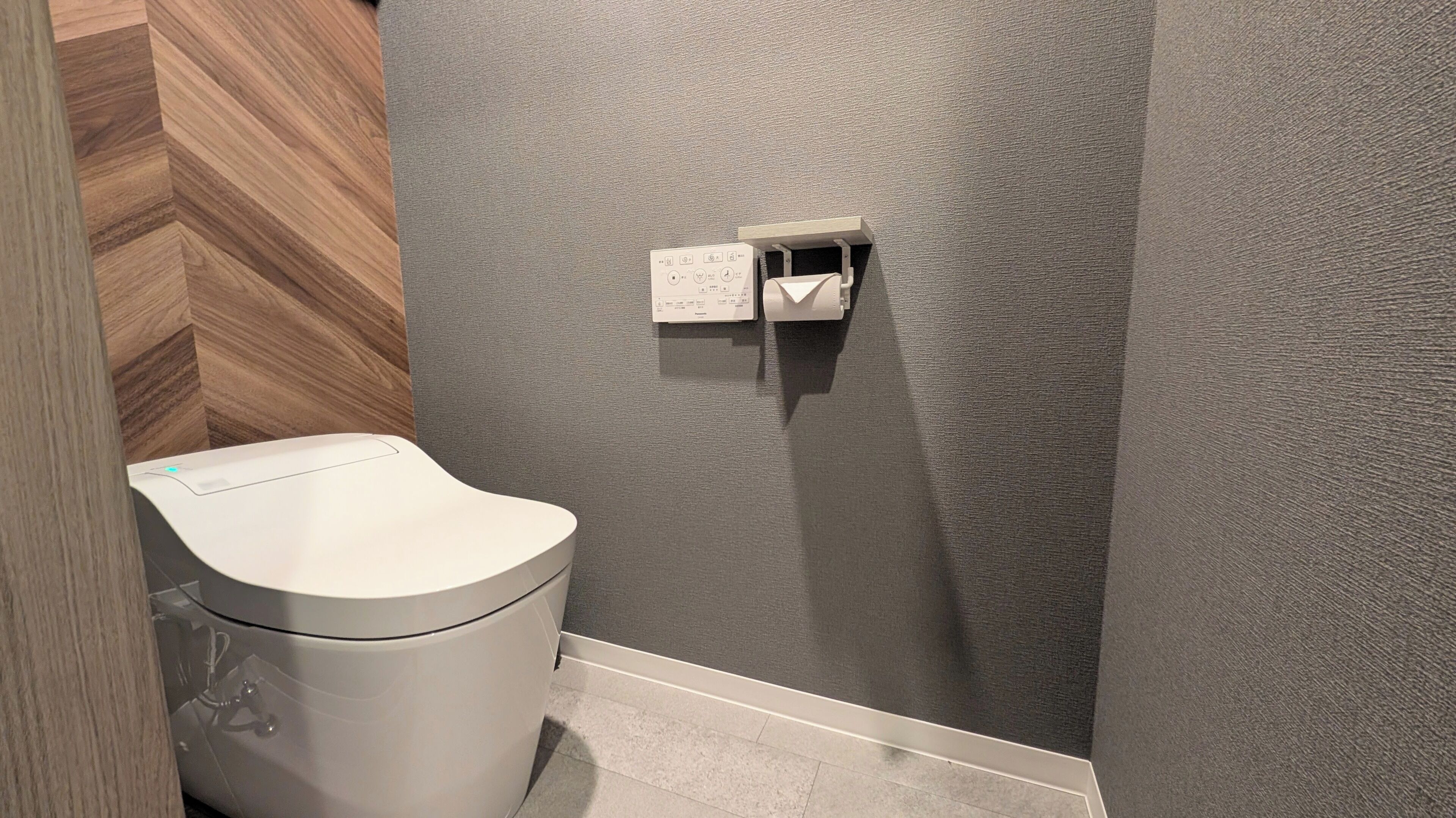 Un baño moderno con inodoro, dispensador de toallas de papel y pared texturizada.