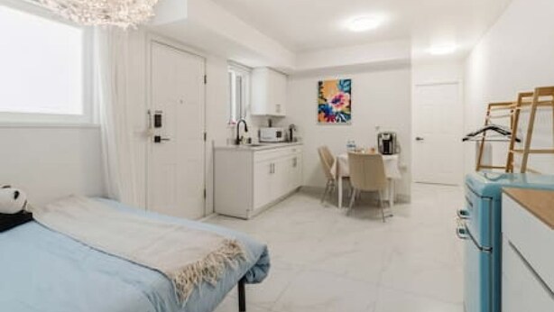 Een slaapkamer met een bed, een bureau, een stoel, een kitchenette en een schilderij aan de muur.