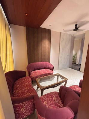 A room with a ceiling fan, a wooden coffee table, and two patterned armchairs. - Corporate Hotel Shivpuri (Shivpuri)