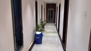 Un pasillo con suelo de mármol, plantas en macetas y un bote de basura azul.