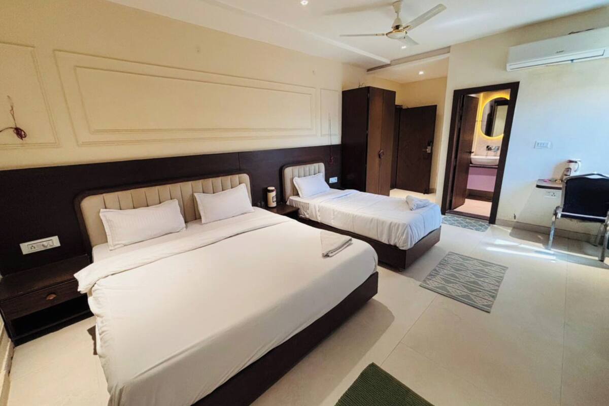 A hotel room with two beds, a ceiling fan, an air conditioning unit, and a small desk with a chair.