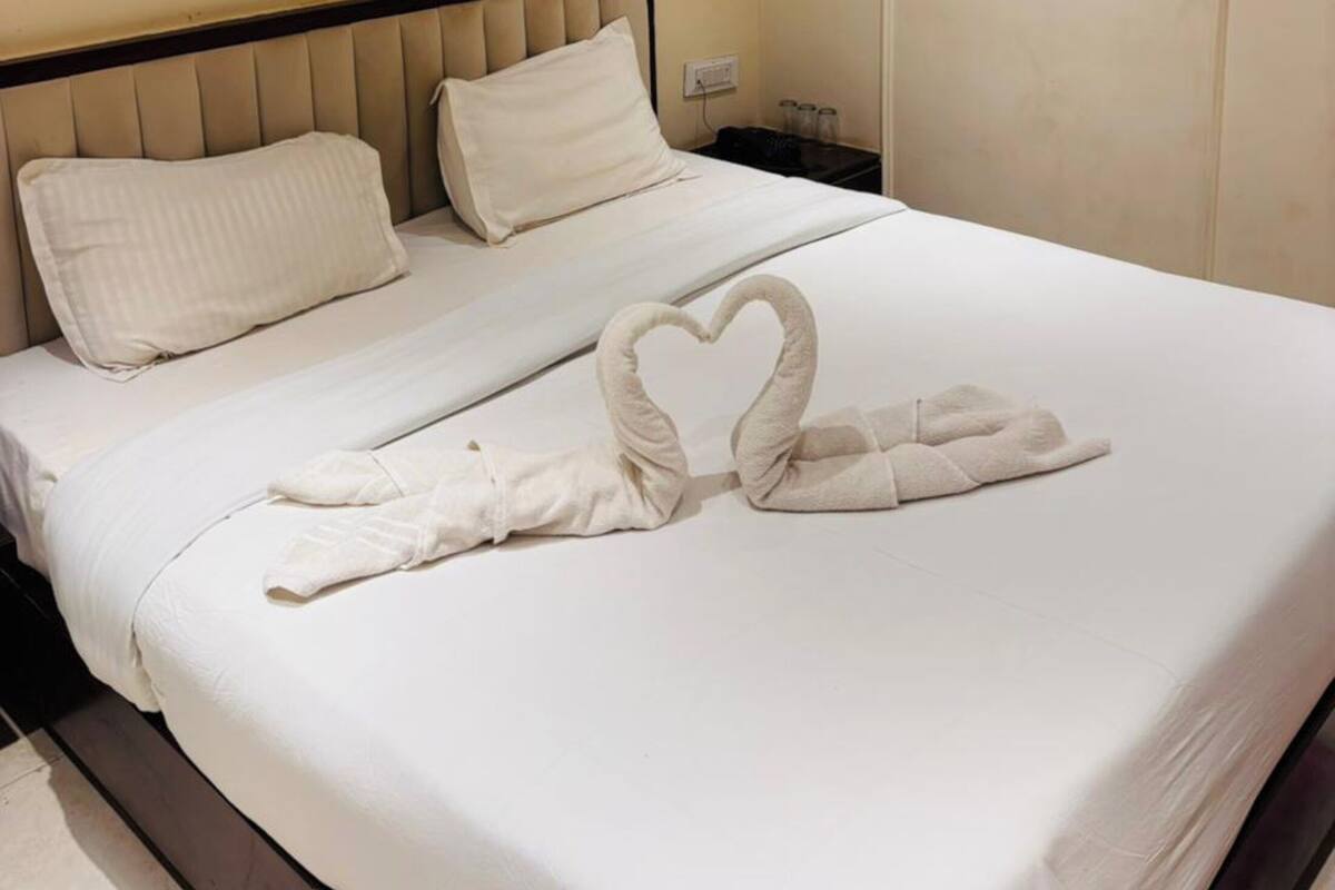 A hotel room with a bed, pillows, a heart-shaped towel arrangement, and a closed door.