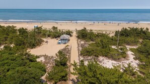 Une vue aérienne d’une plage avec un petit bâtiment, un ciel dégagé et l’océan en arrière-plan.