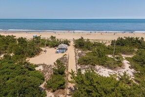 Eine Vogelperspektive eines Strandes mit einem kleinen Gebäude, blauem Himmel und dem Meer im Hintergrund.
