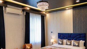 A hotel room with a large bed, a small table, a chair, and a chandelier. - ELIVAAS Signature Raj Farms | 3 BHK Villa with Pvt Pool (Gurugram)