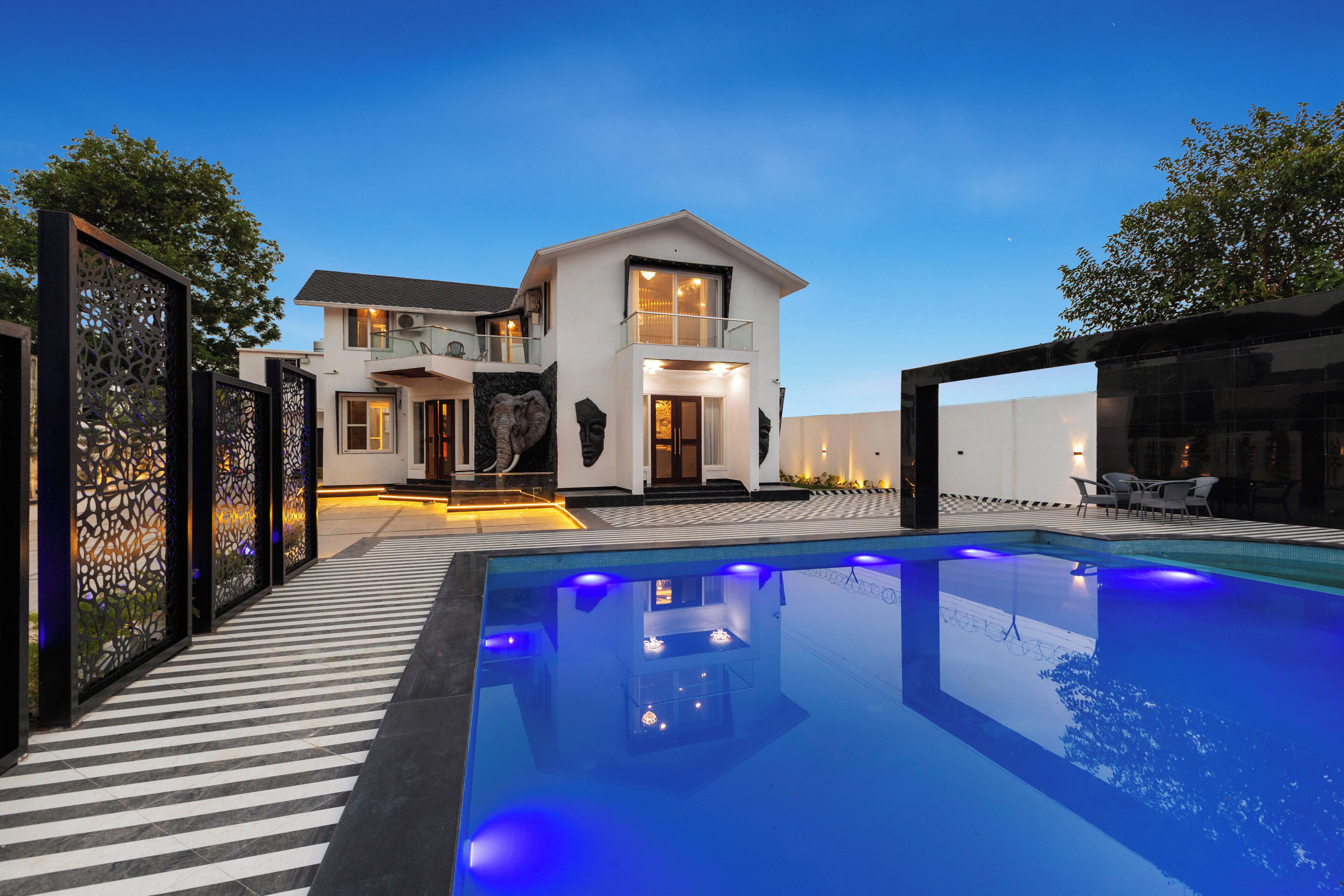 A modern house with a swimming pool, a balcony, and a well-lit entrance.
