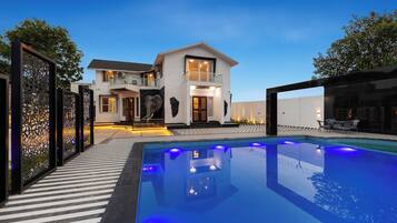 A modern house with a swimming pool, a balcony, and a well-lit entrance.